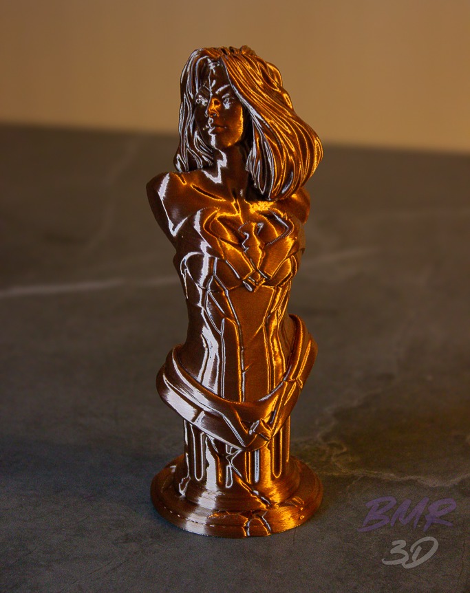 Busto feminino impresso em 3D em filamento cor de cobre, sobre superfície escura, com luz lateral revelando as camadas