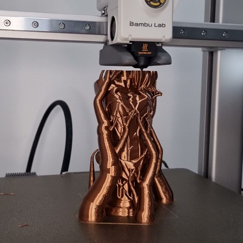 Busto em filamento cor de cobre sendo impresso na Bambu Lab A1, com o bico logo acima da peça