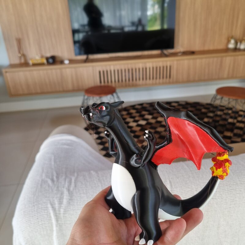 Dragão impresso em 3D em preto, vermelho e branco, segurado na palma da mão
