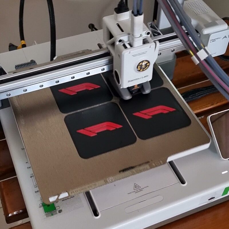 Quatro peças pretas com detalhe vermelho sendo impressas ao mesmo tempo na Bambu Lab A1