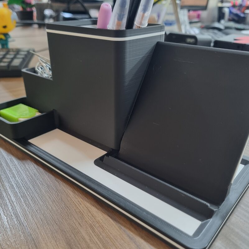 Organizador de mesa impresso em 3D em filamento preto, sobre mesa de madeira