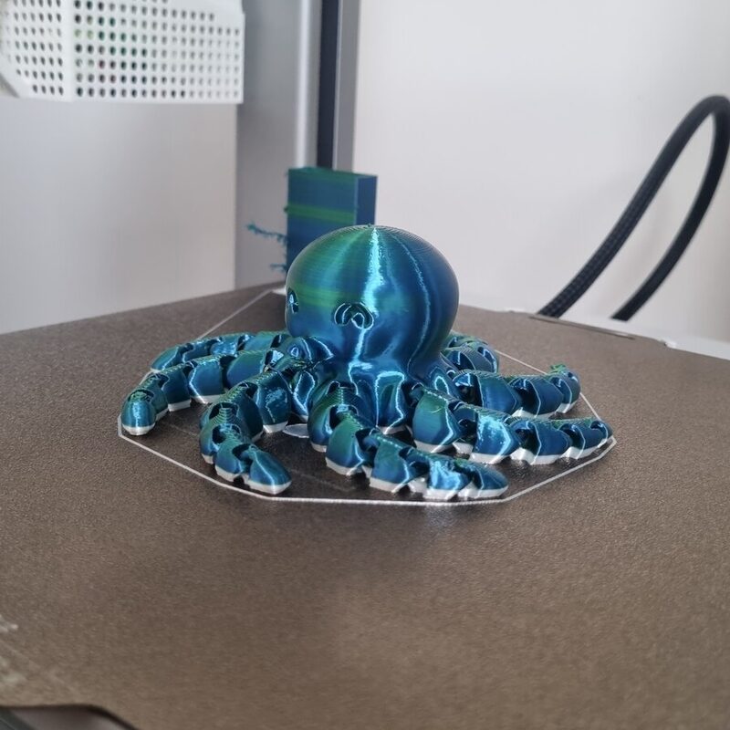 Polvo articulado impresso em filamento azul e verde, ainda sobre a mesa de impressão